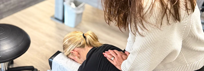 A person is lying face down on a chiropractic table while another person applies pressure to the upper back, performing a spinal adjustment.
